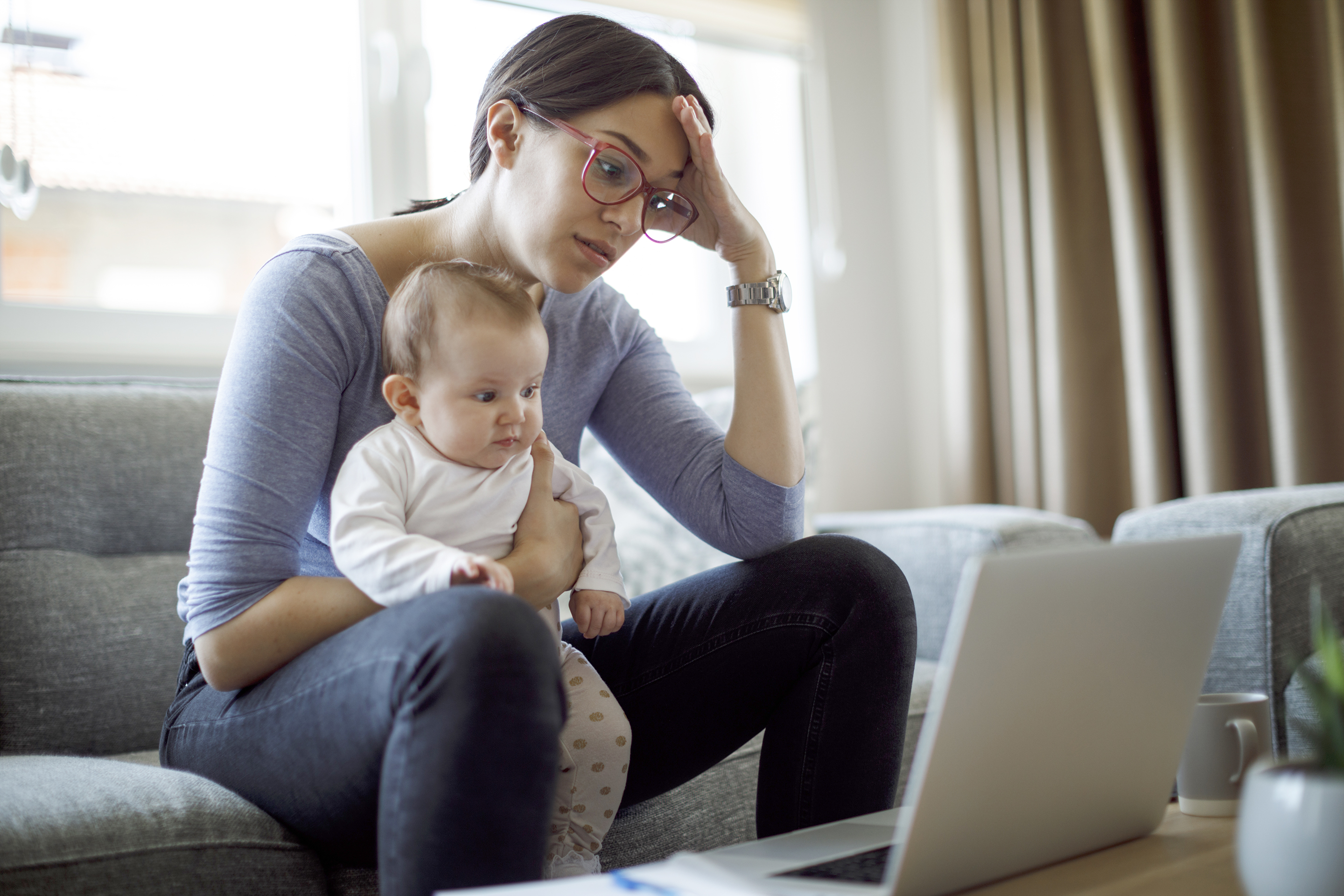 Mom with eyeglasses sits on couch a holds baby in her lap