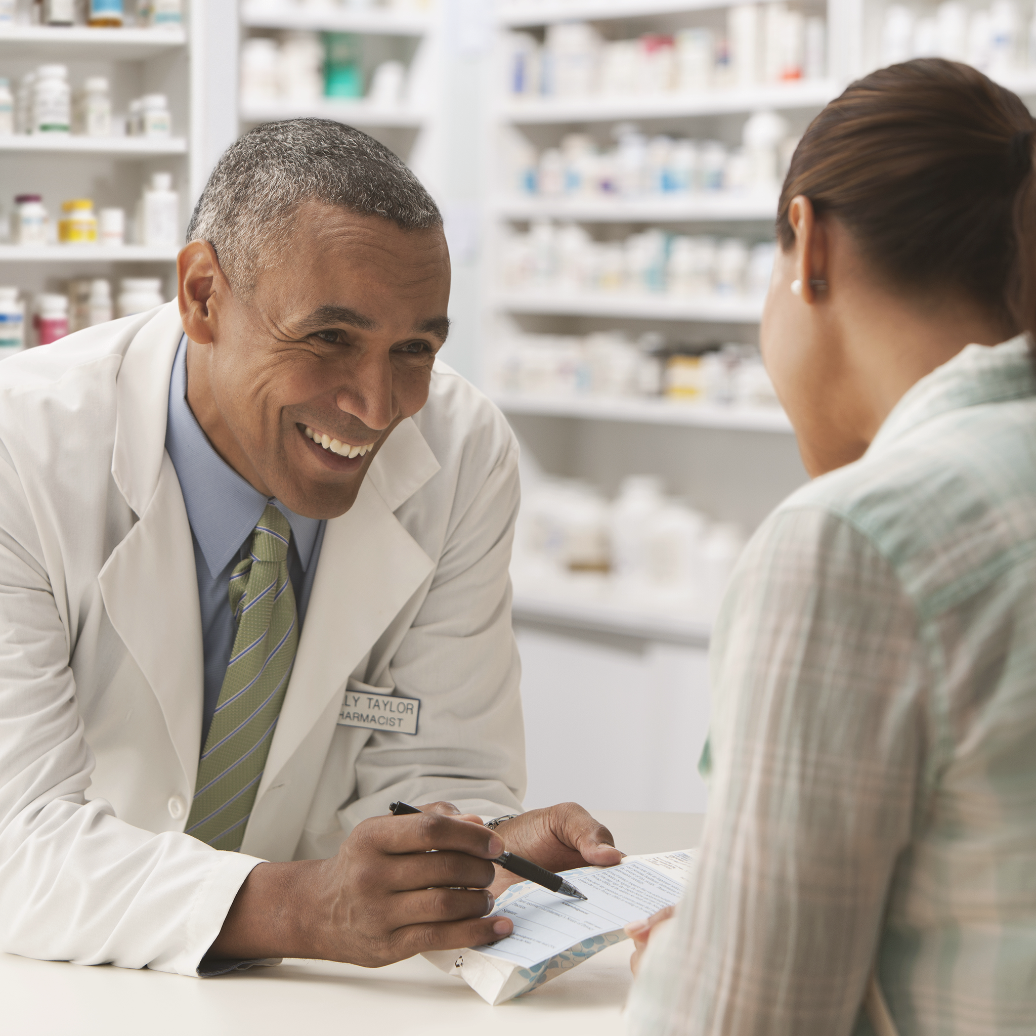 Smiling pharmacist shows customer his or her or their prescription