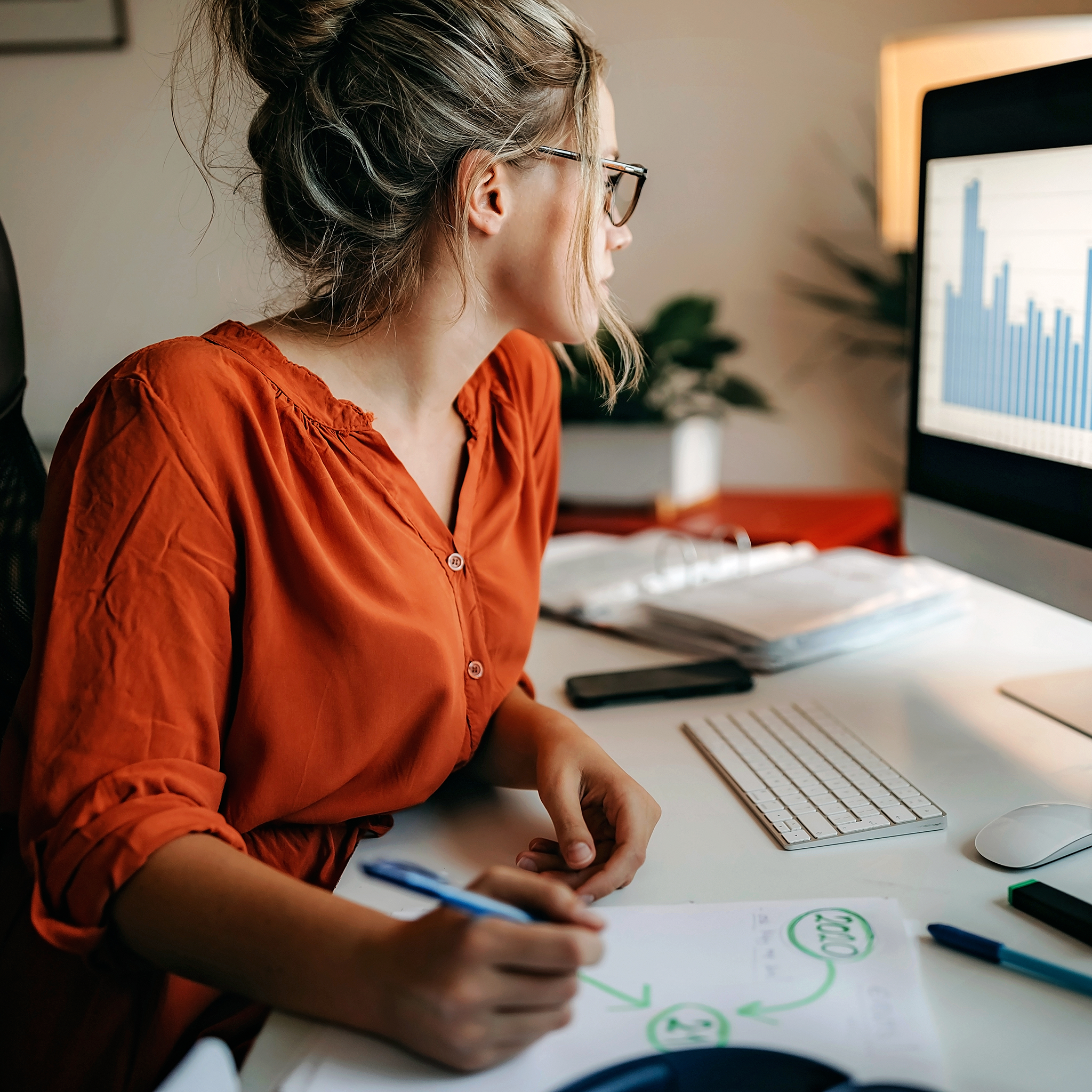 Woman looks at blue bar graphs on computer screen inside office