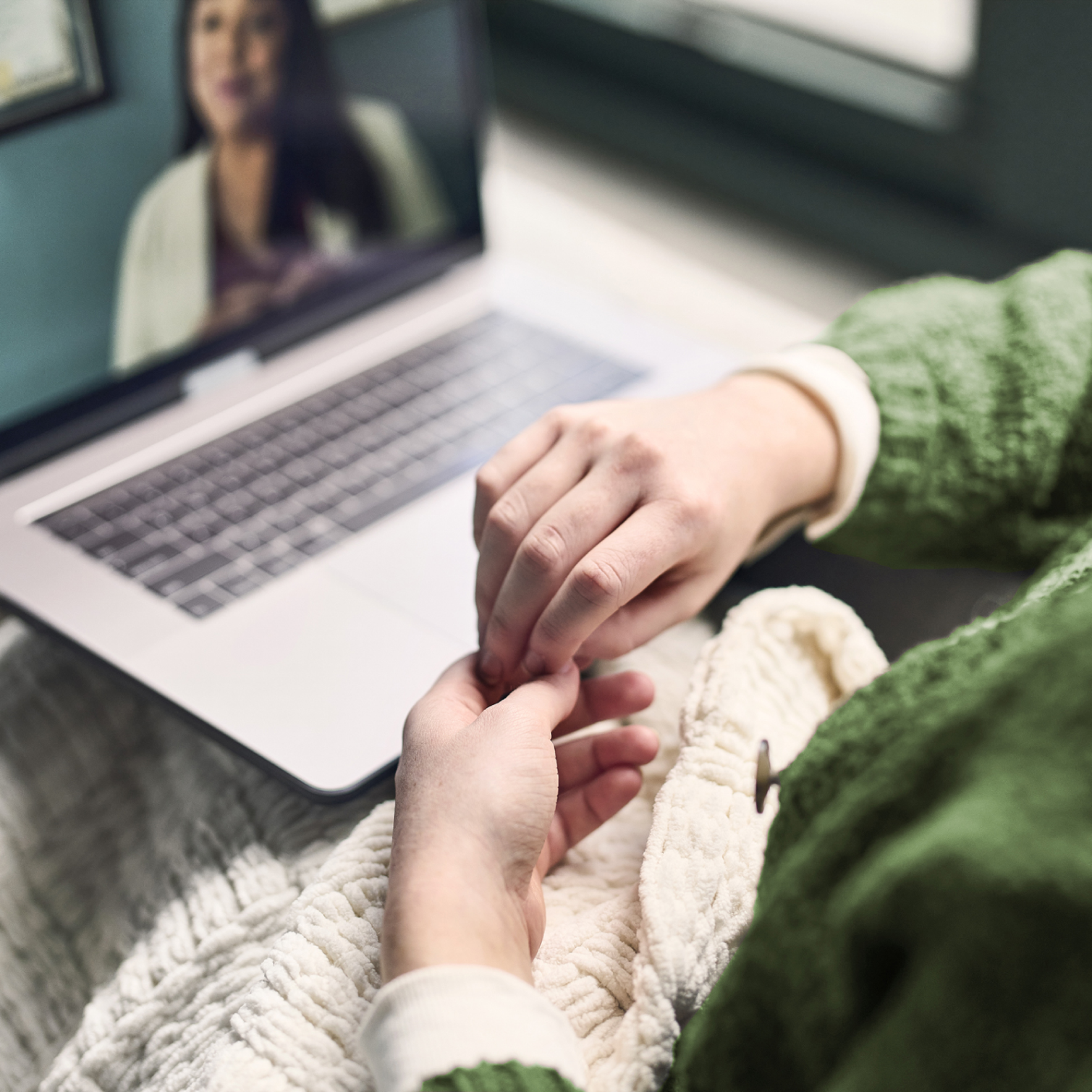 Pair of hands folded in front of telehealth appointment on laptop screen