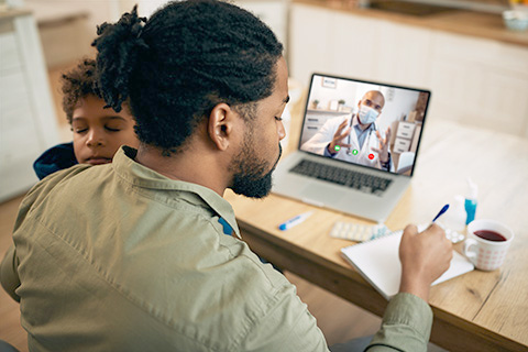 Man with child talking to doctor virtually on laptop