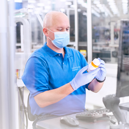 Man in blue shirt sits at computer and places label on prescription bottle