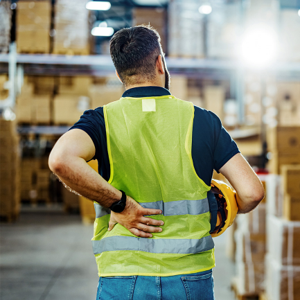 Warehouse worker in pain places hand on lower back