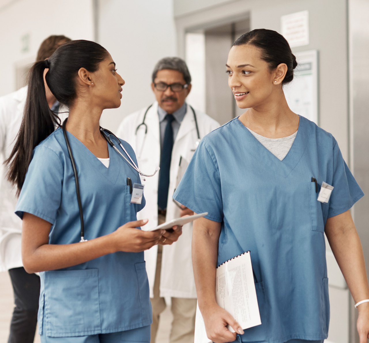 Two medical professionals wearing scrubs walk and talk together