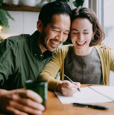 man and woman smiling while writing in a notepad