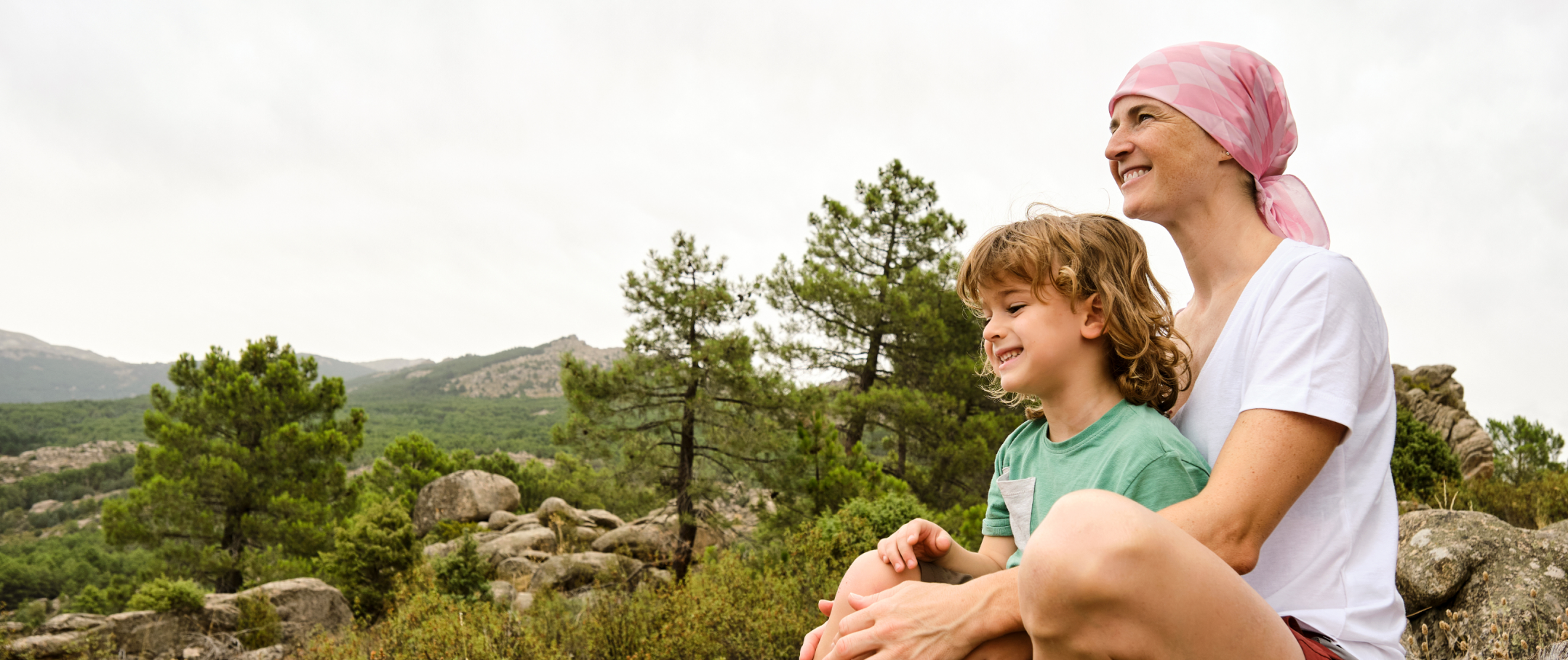 A cancer patient wears a kerchief and embraces a child outdoors