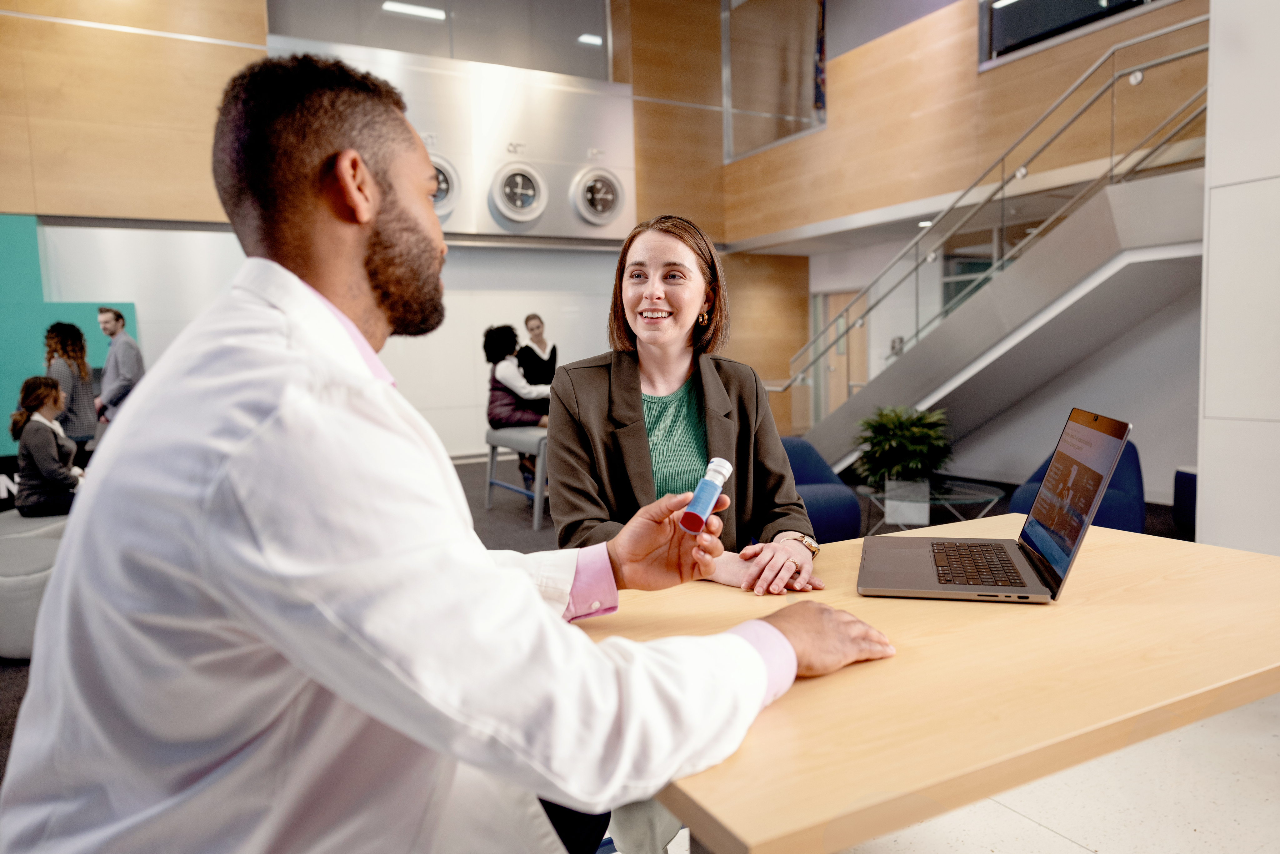 Male in lab coat talking with female at desk