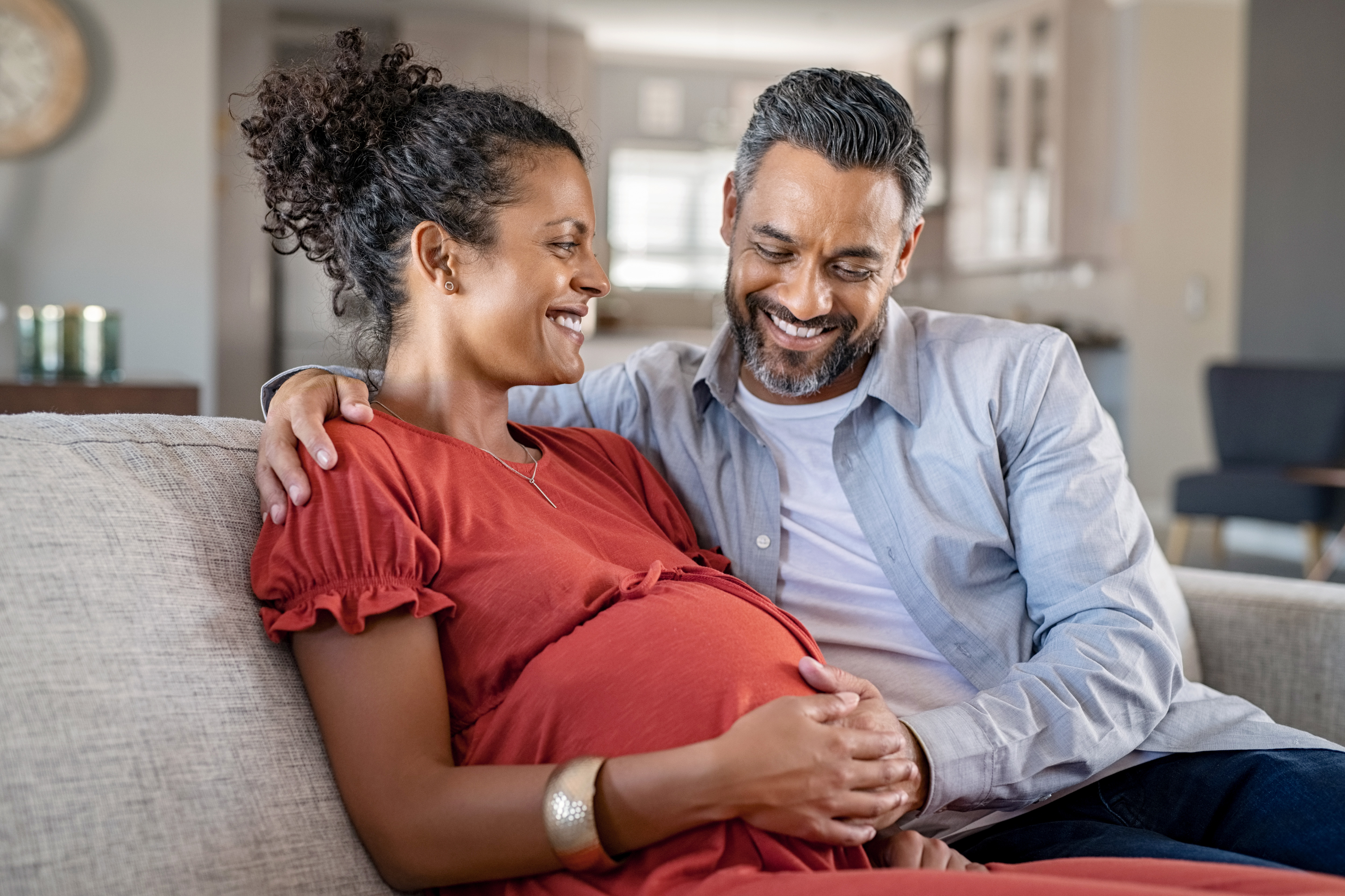 Mature pregnant couple on couch smiling