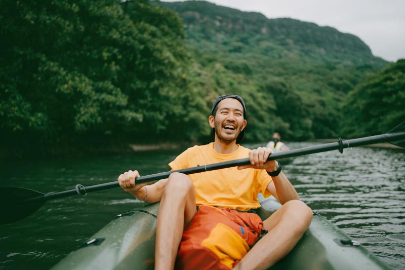 Smiling man wearing orange is on a river in a kayak.