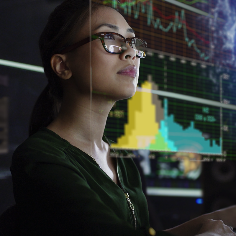 Bespectacled woman looks off in distance in front of large data visual