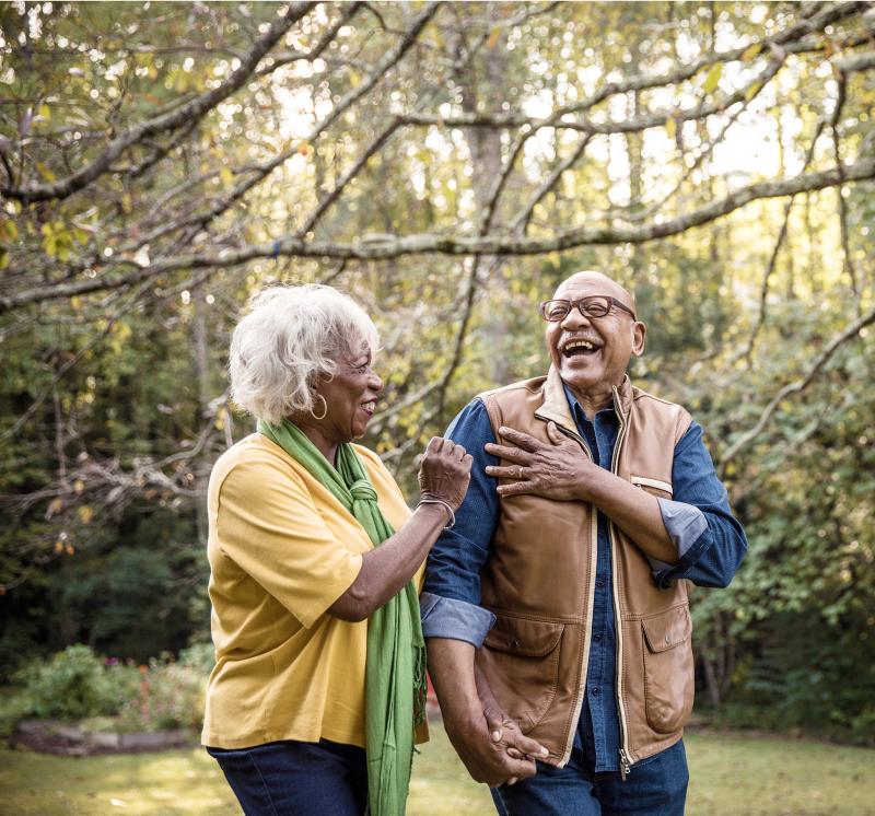 Older man and woman outdoors holding hands and laughing.