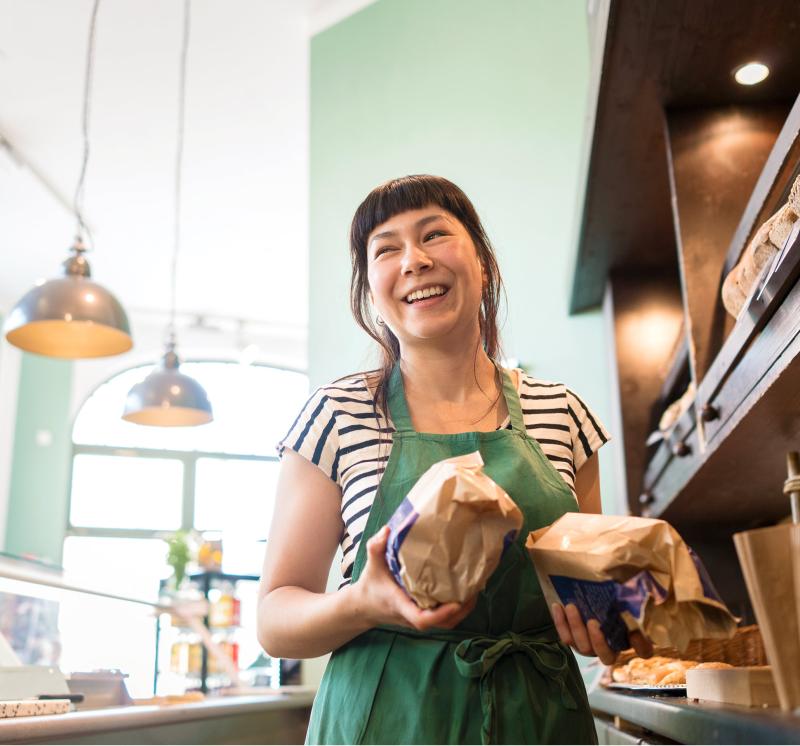 Smiling woman wearing an apron and standing behind the counter at a bakery.