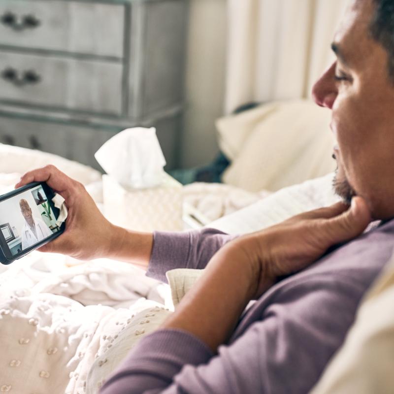 Man sits in bed for telemedicine appointment on this smart phone