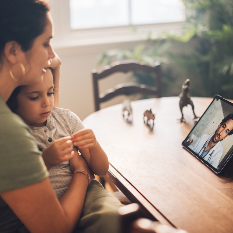 Woman holds child in arms during a telehealth appointment at home