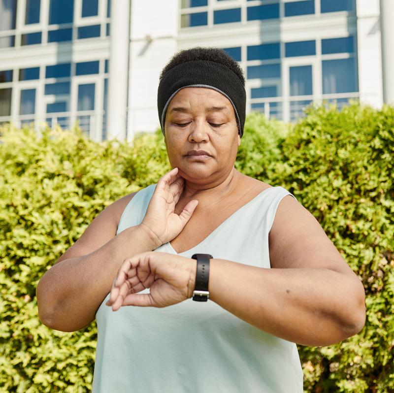 Woman looking down and listening to her pulse while timing it with wrist watch