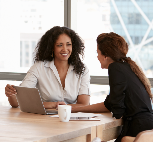 Two smiling women sitting down in well lit room