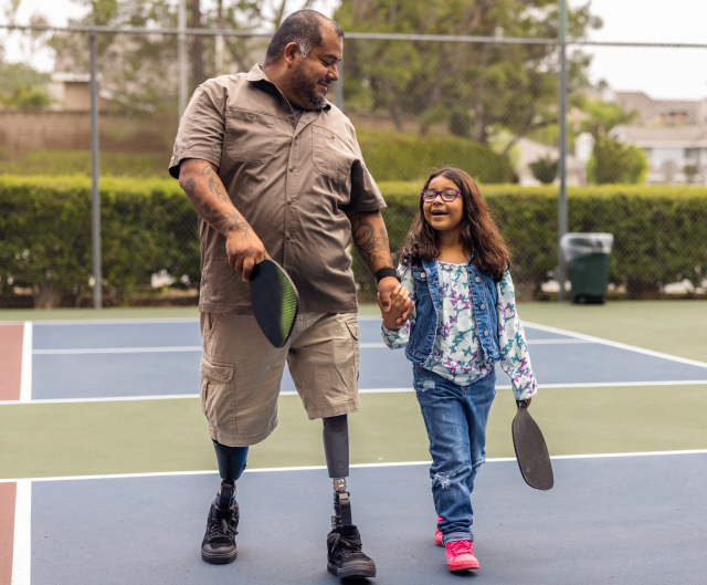 Father with prosthetic legs escorts young daughter from pickleball court