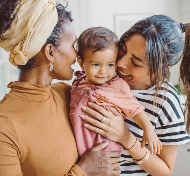 Happy infant held and hugged between two happy women