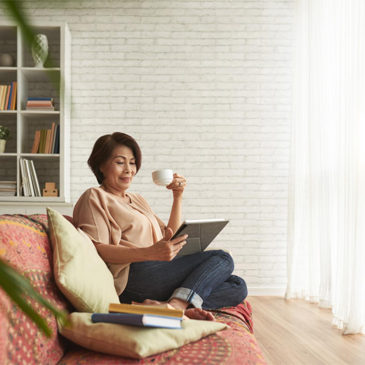 Woman holds tea cup and looks down at tablet