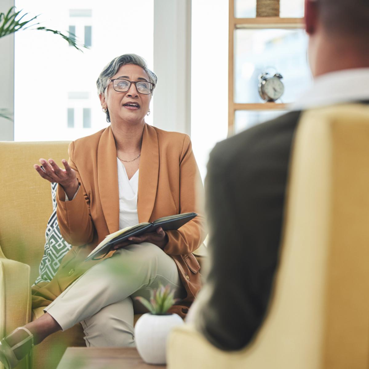 Woman with eyeglasses and blazer holds an open book on her lap