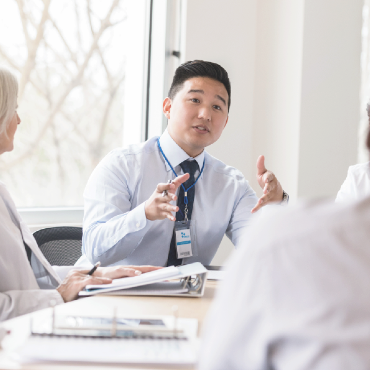 Man sits at desk and is surrounded by colleagues